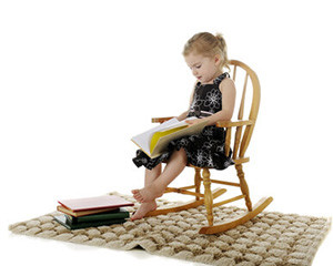 Kleines Mädchen sitzt im Kinder-Schaukelstuhl und erfreut sich an Büchern
