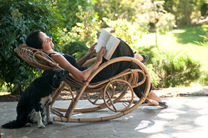Junge Frau entspannt lesend im Garten-Schaukelstuhl